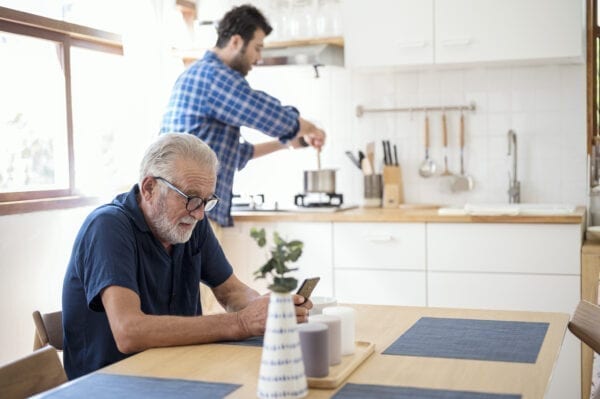 Father waiting some meal from his son. Son cooking in background while father using smartphone waiting patiently. Weekend Activity, Simply Living.