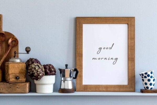 Kitchen shelf decorated with photo frame, wooden cutting board, coffee maker, and cups