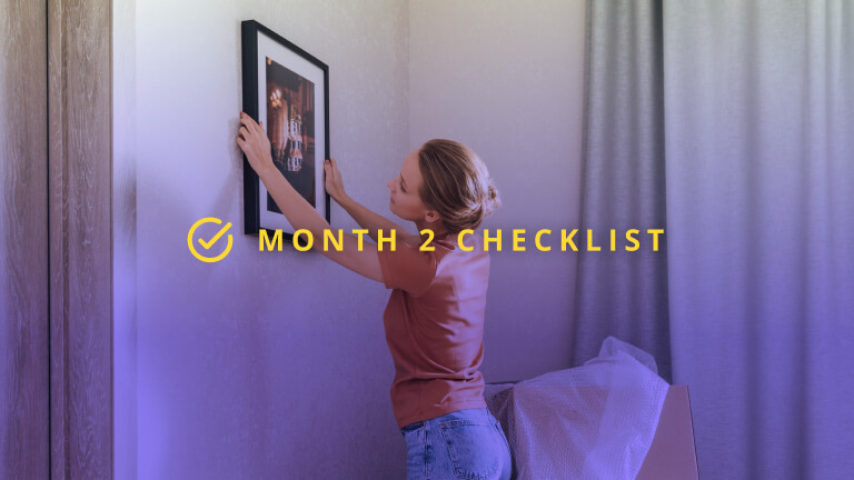 Young woman putting picture frame on wall at new home