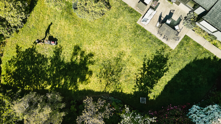 Aerial view of man cutting grass in backyard of home