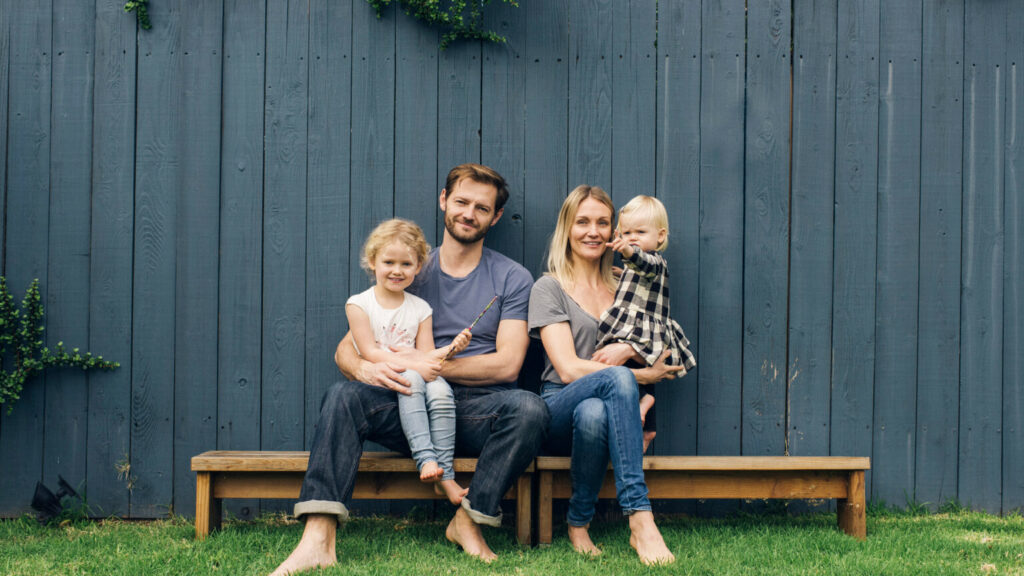 Full length portrait of happy parents and children sitting on seats against fence at yard