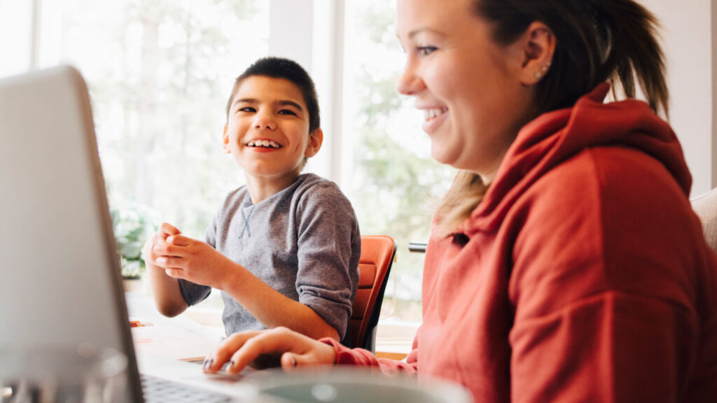 Mother using laptop while sitting with happy autistic son in living room at home