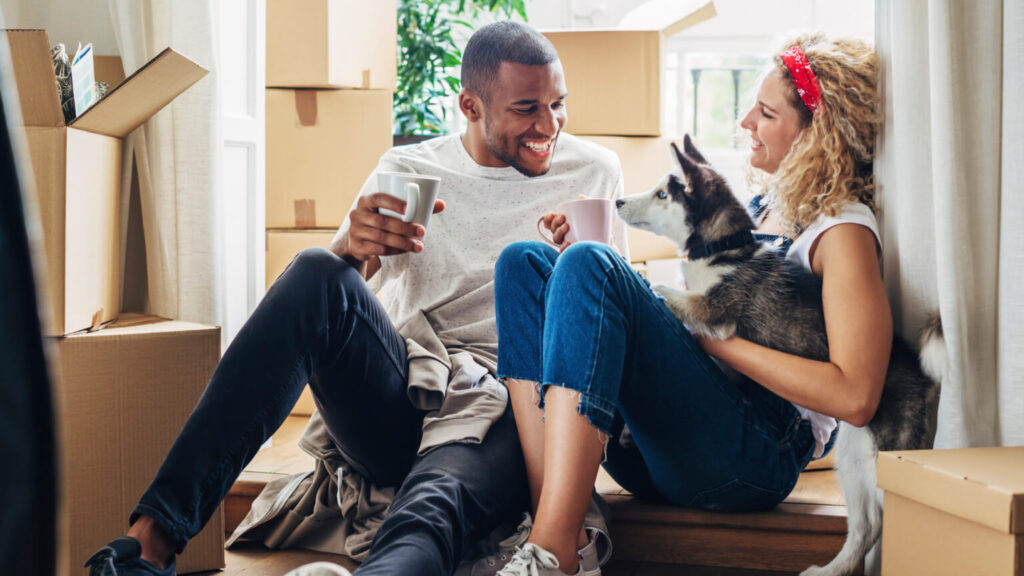 Happy couple playing with dog while sitting at doorway in new house