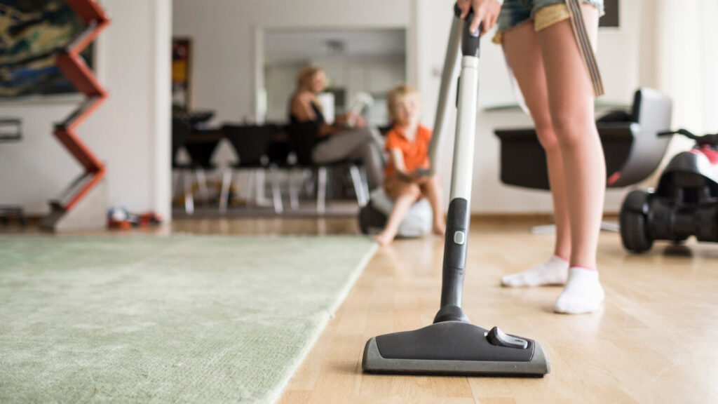 Low section of girl cleaning floor with vacuum cleaner at home