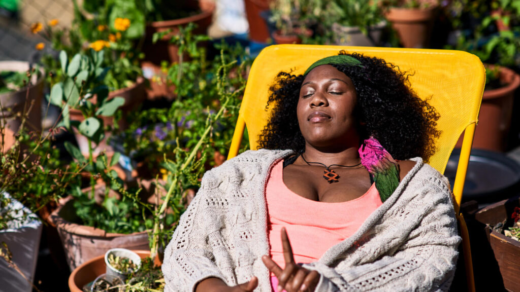 Serene black woman in her 30s relaxing on roof terrace, raising finger so as not to be disturbed, serenity, tranquility, peace and quiet, relaxation