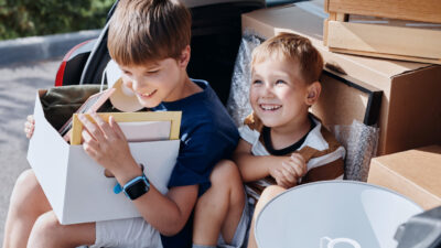 Portrait of two smiling boys sitting in car trunk with boxes while moving into new house