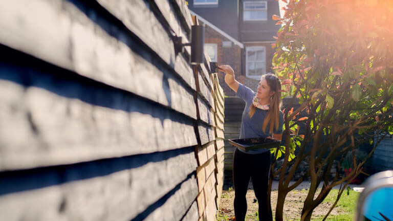 Young woman painting garden fence in the sun