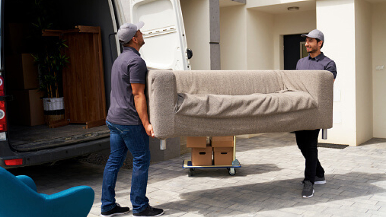 Male delivery coworkers unloading sofa from moving van near house
