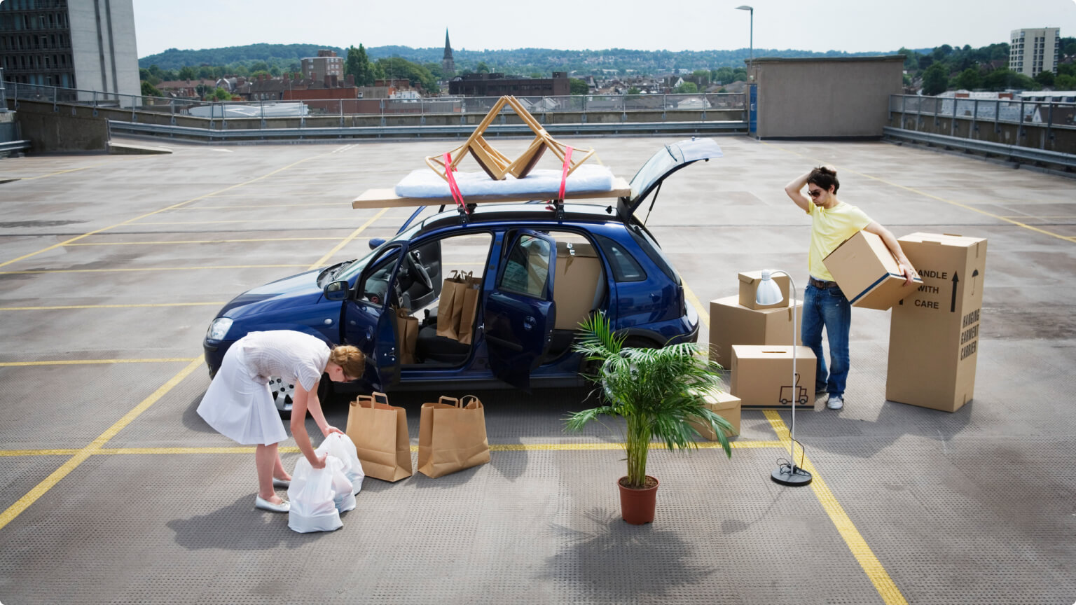 Young couple loading boxes and bags into car on rooftop carpark