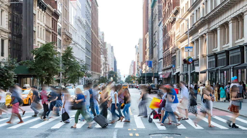 Busy street scene in New York City with groups of people walking across a crowded intersection on Fifth Avenue