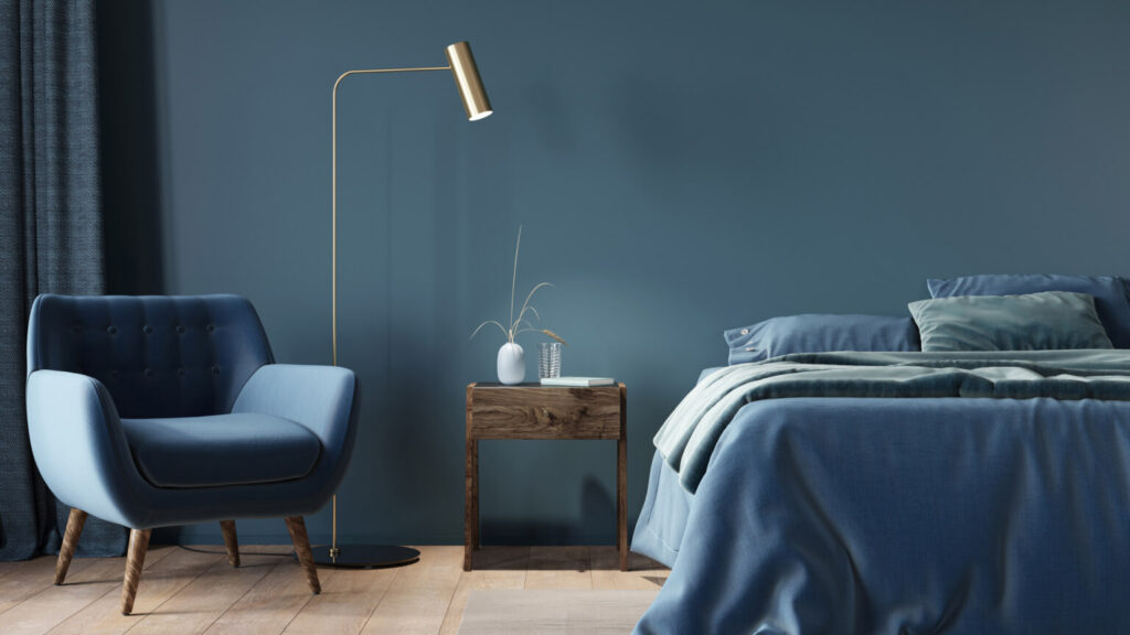 Bedroom in dark blue with a wide bed, a wooden nightstand and a golden floor lamp