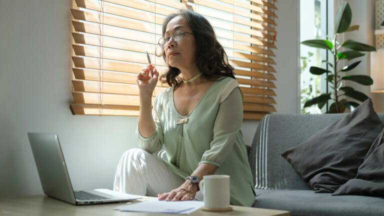 Beautiful senior woman using laptop and relaxing on couch in cozy living room. Retired life concept.