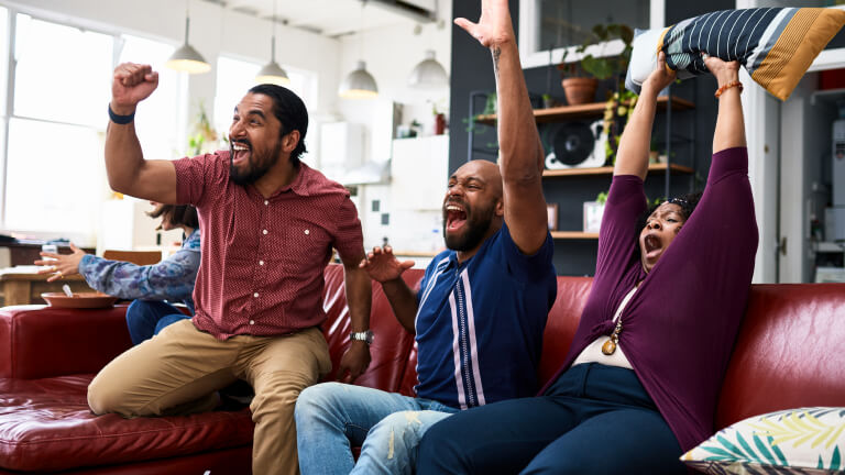 Friends watching TV at home and cheering with arms raised